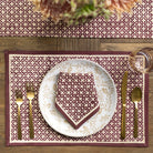 Dining table setting with a patterned placemat, plate, and cutlery on a wooden surface.