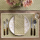 Dining table setting with patterned placemats, plates, and cutlery on a wooden surface.