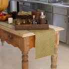 Wooden table with a green runner, candles, and decorative items in a kitchen setting.