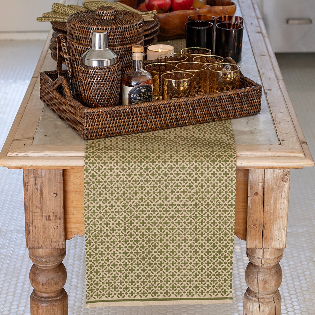 Wooden table with a woven tray containing bar items and a green patterned table runner.