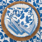 Set of blue and white patterned napkins on a woven plate with a matching tablecloth.