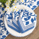 Set of blue and white patterned napkins on a wooden table with floral elements.