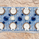 Dining table setting with blue and white patterned tablecloth, plates, bowls, and candles.