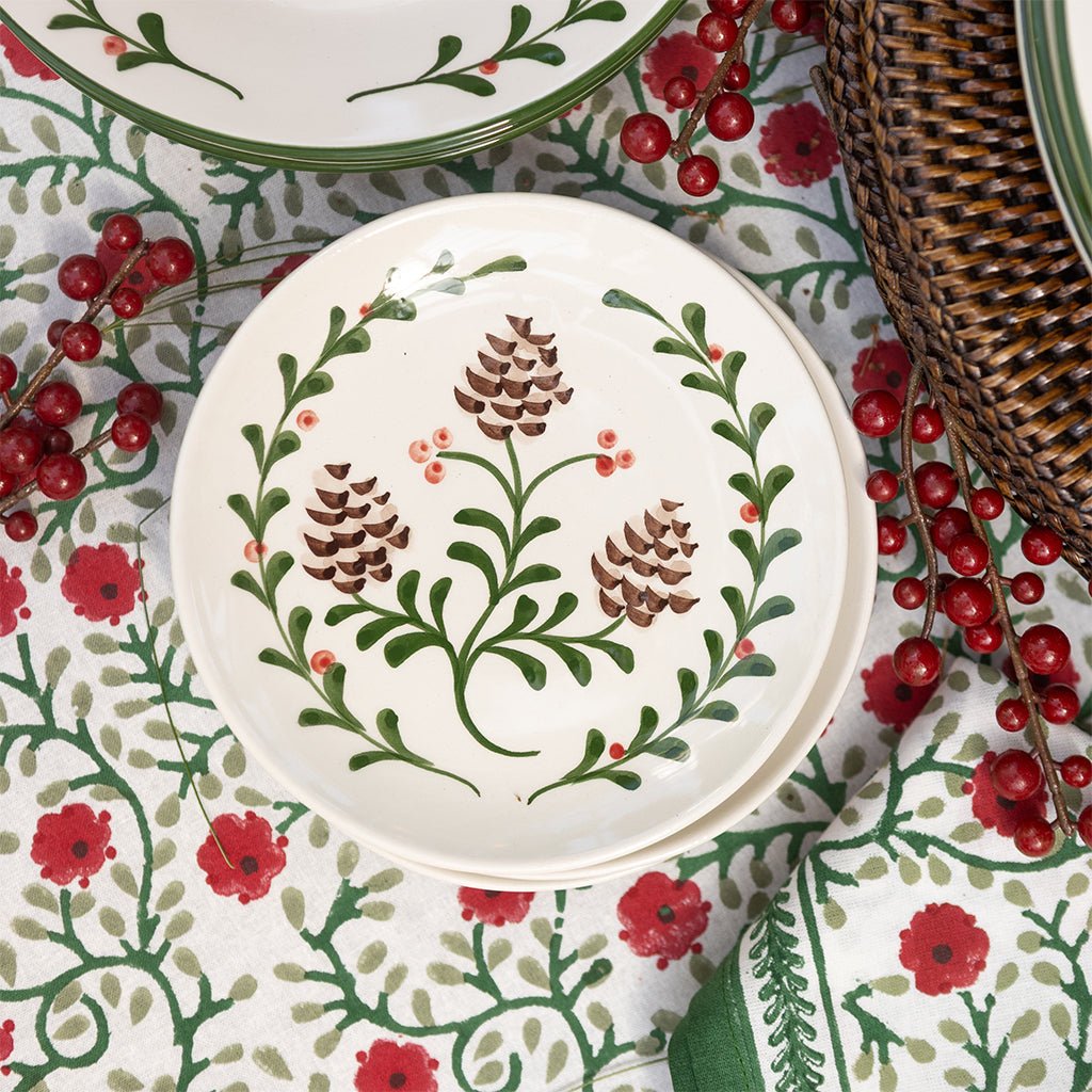 Decorative plate with pine cones and holly patterns on a tablecloth with red berries and flowers.
