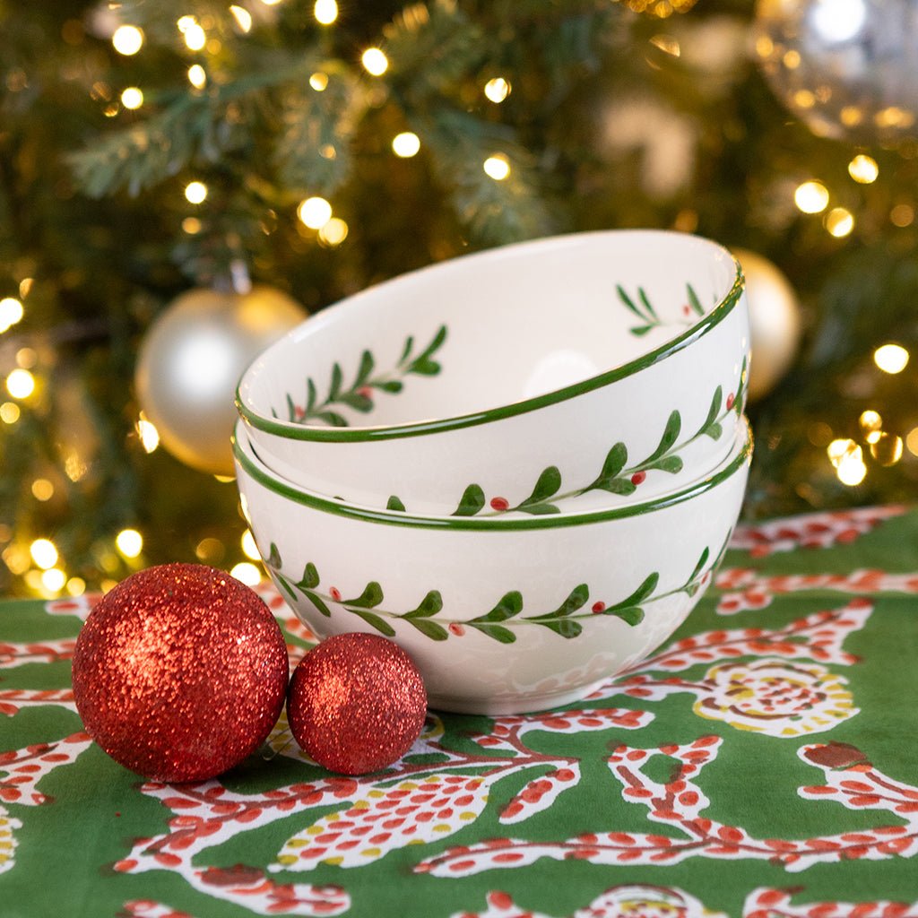 Stack of white bowls with green patterns on a festive tablecloth with Christmas decorations.
