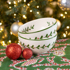 Stack of white bowls with green patterns on a festive tablecloth with Christmas decorations.