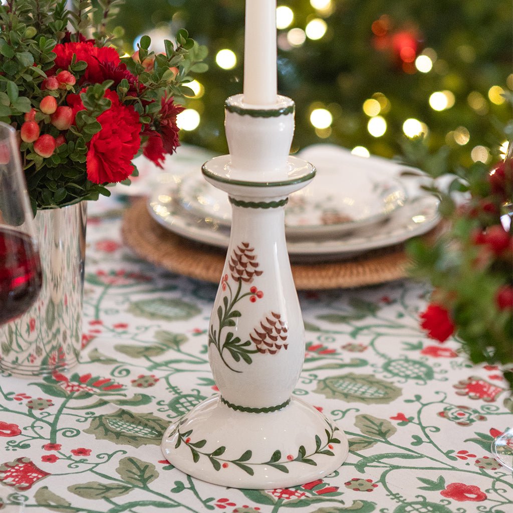 Decorative candlestick with floral patterns on a tablecloth with floral designs, Christmas tree in the background.
