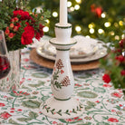 Decorative candlestick with floral patterns on a tablecloth with floral designs, Christmas tree in the background.