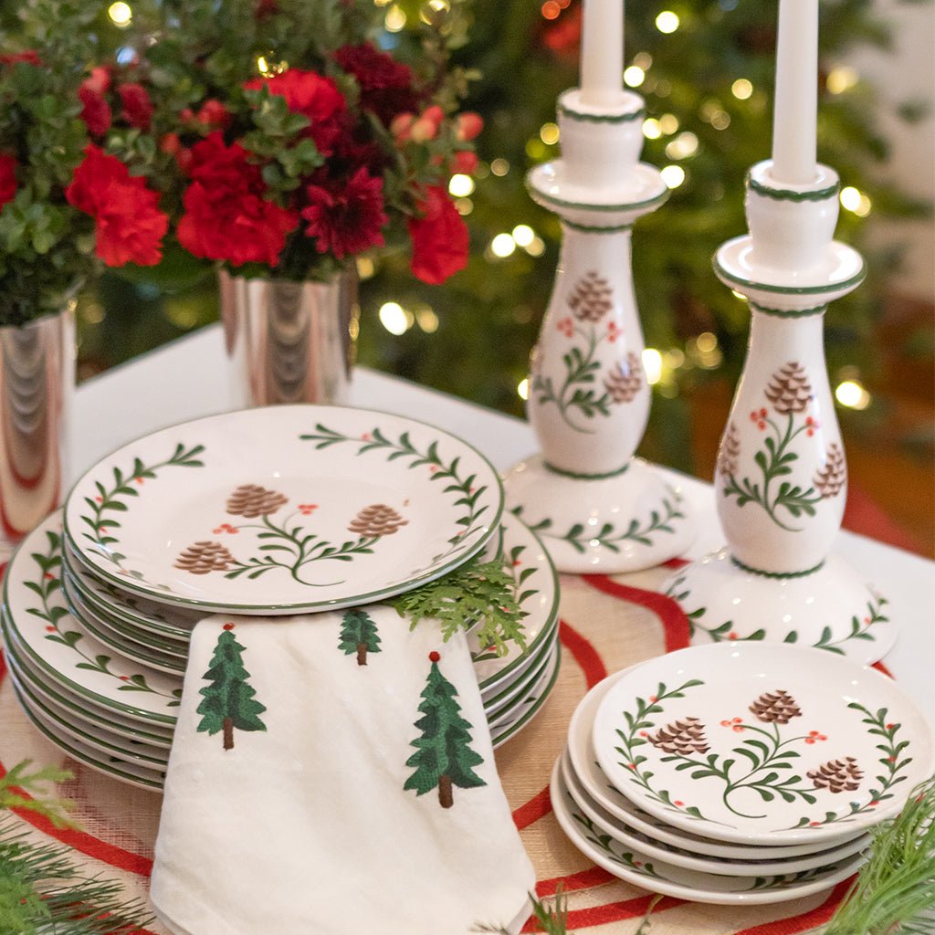 Decorative Christmas plates with tree and pine cone patterns on a table with candles and flowers.