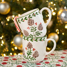 Two stacked mugs with Christmas-themed design in front of a decorated tree.