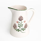 White ceramic pitcher with floral and pine cone design on a white background