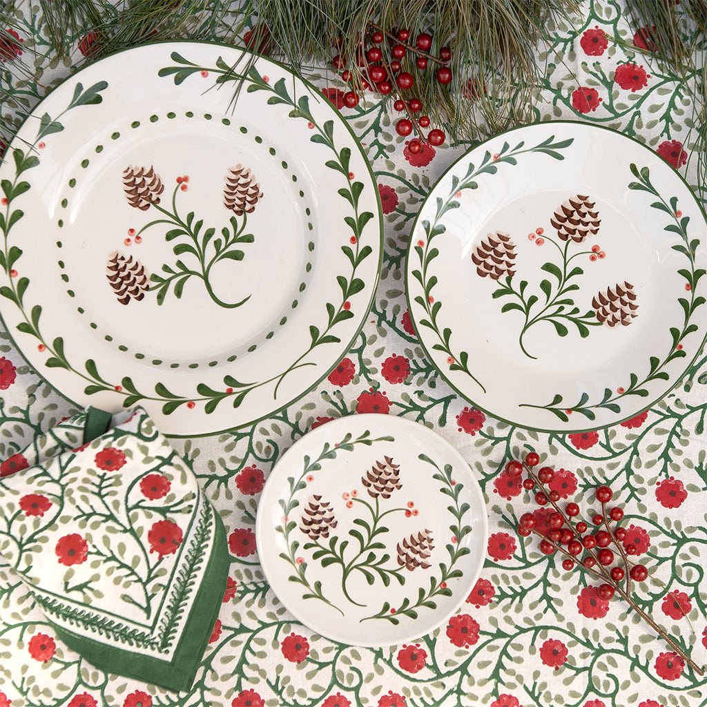 Set of ceramic plates with floral and pine cone design on a patterned background.