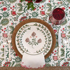 Decorative table setting with floral-patterned plates, cutlery, and a red glass on a matching tablecloth.