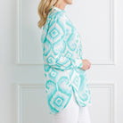 Woman wearing a turquoise and white patterned jacket against a white wall.