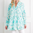 Woman wearing a turquoise and white patterned blouse against a white background
