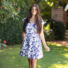Woman wearing a blue and white patterned dress standing outdoors with greenery in the background