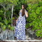 Woman in a blue and white patterned dress standing among green foliage.