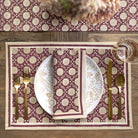 Table setting with floral-patterned placemat, plates, cutlery, and glass on a wooden table.