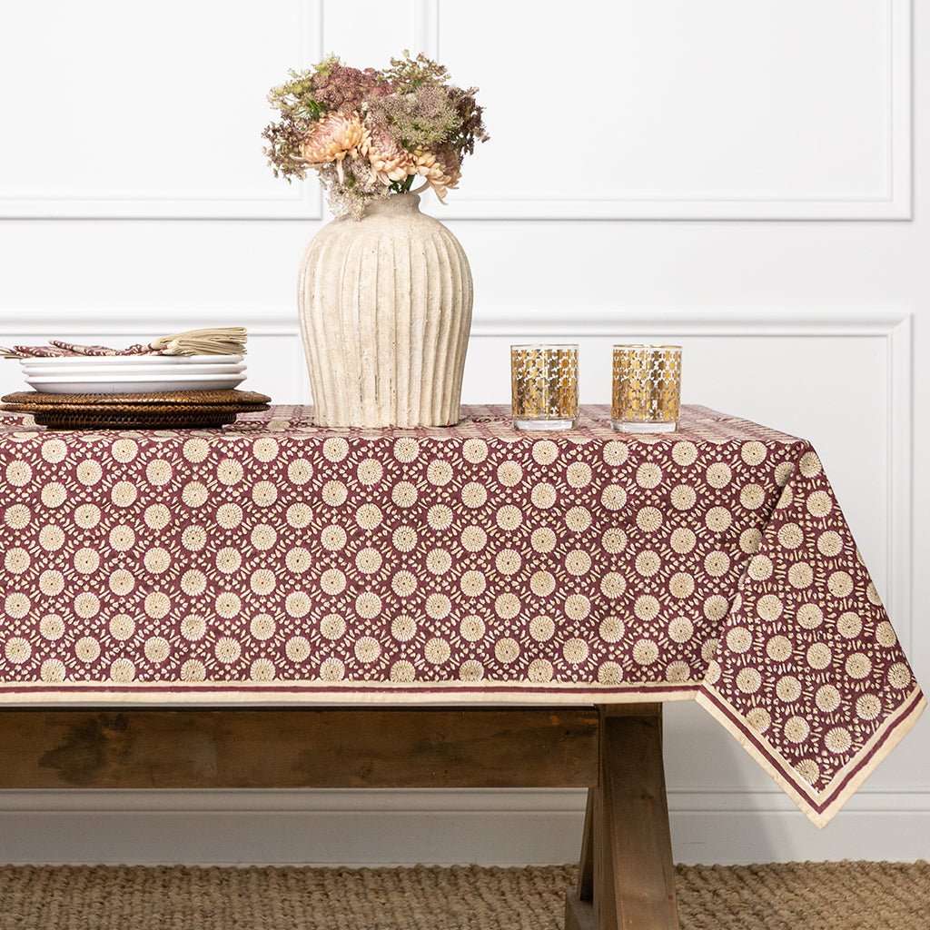 Table with a patterned tablecloth, vase with flowers, and glasses on a neutral background