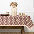 Table with a patterned tablecloth, vase with flowers, and glasses on a neutral background