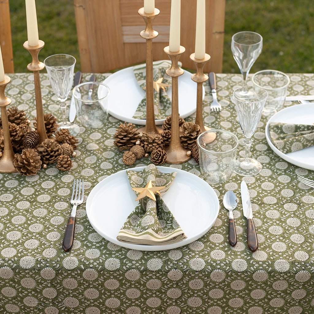 Decorative table setting with candles, pinecones, and patterned tablecloth.