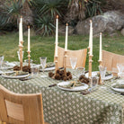 Elegant outdoor table setting with candles, glasses, and patterned tablecloth.
