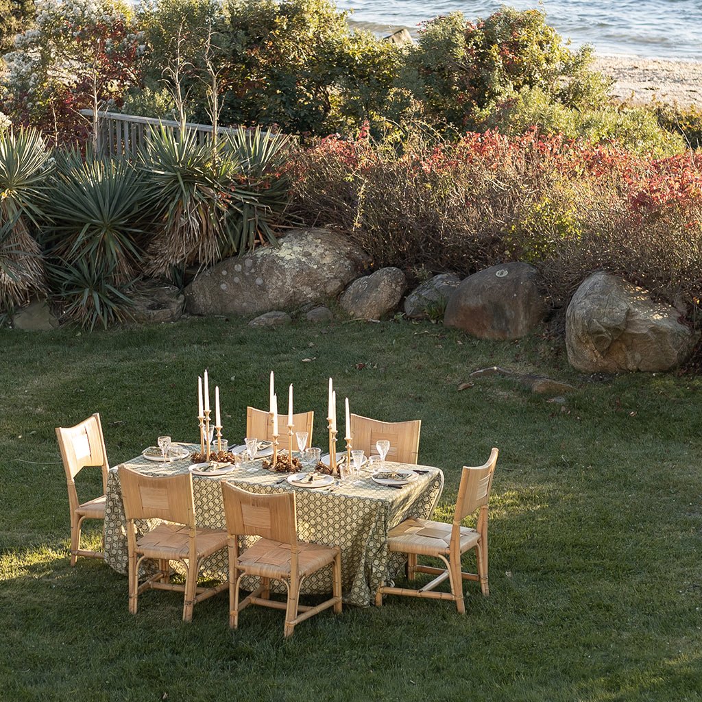 Dining table set for a meal outdoors with chairs and candles, surrounded by nature.