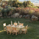 Dining table set for a meal outdoors with chairs and candles, surrounded by nature.