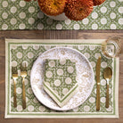 Table setting with green and white patterned placemat, plate, and napkin on a wooden table.