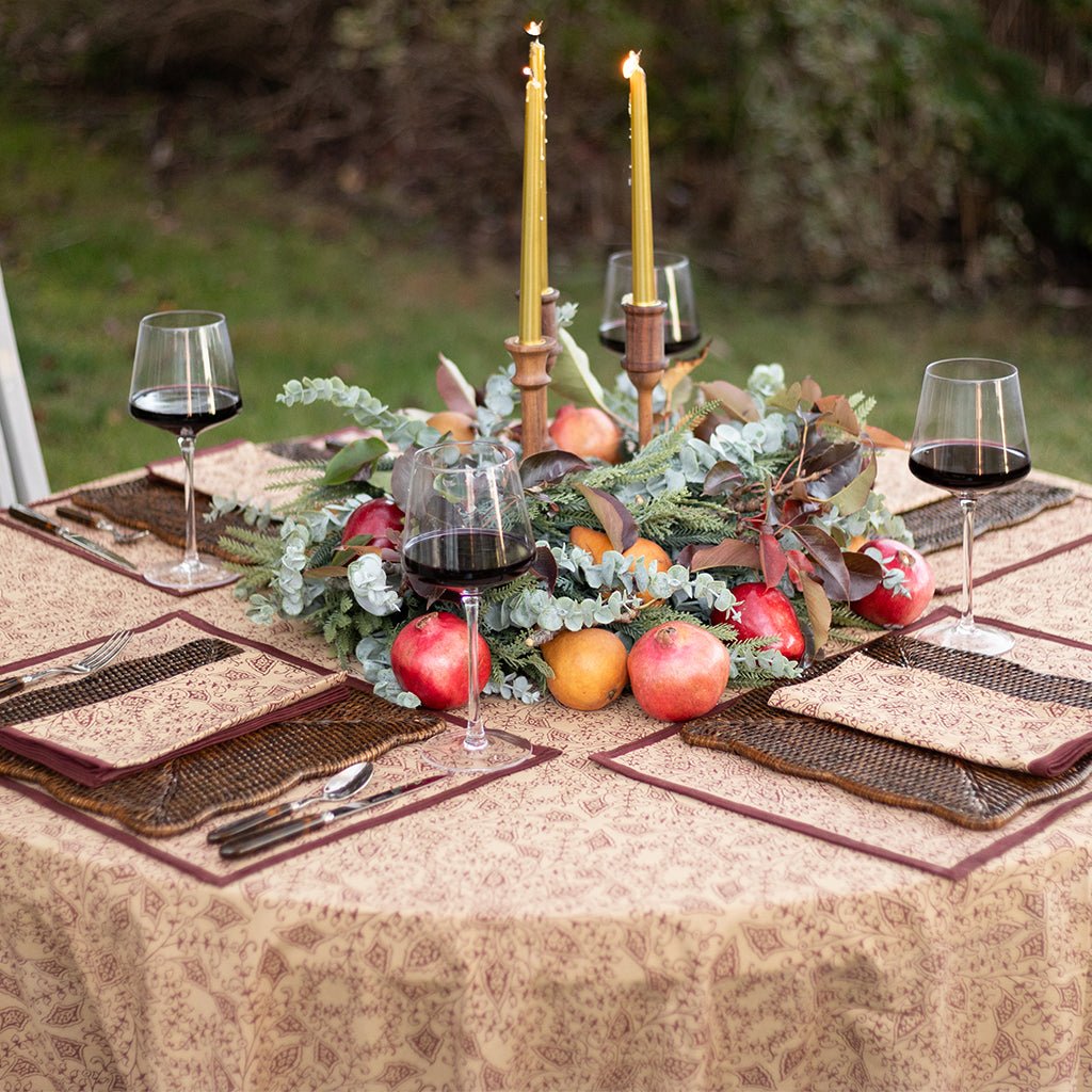 Decorative table setting with candles, fruits, and glasses on a patterned tablecloth.