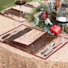 Set table with patterned placemats, cutlery, and wine glasses on a decorative tablecloth.