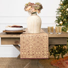 Decorative table setting with a vase, plates, and glasses on a wooden table in front of a Christmas tree.