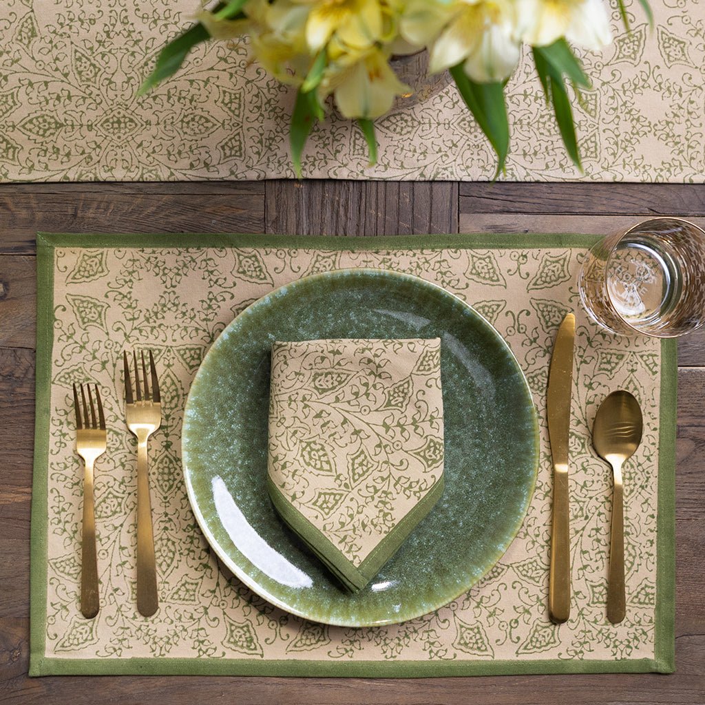 Elegant table setting with green plate, gold cutlery, and patterned placemat on a wooden table.