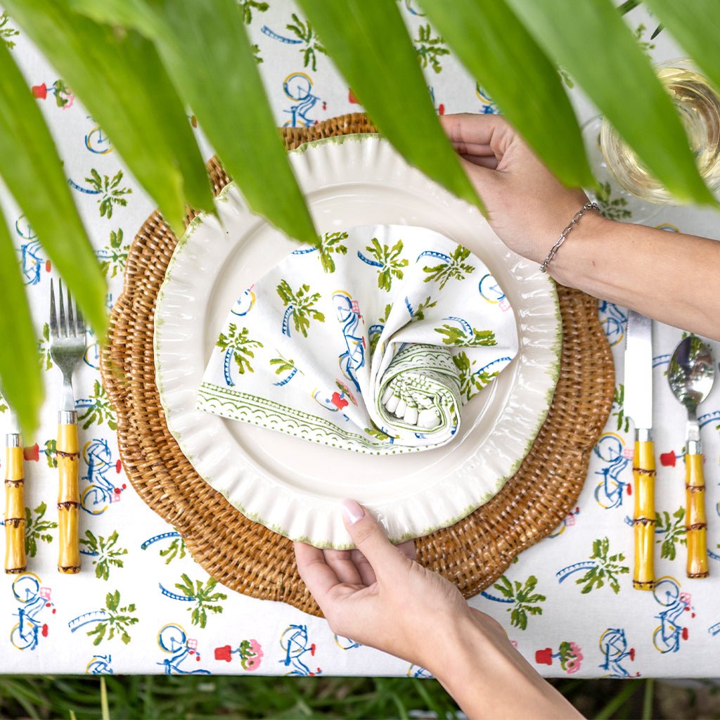 Table setting with a woven placemat, white plate, and decorative napkin on a colorful tablecloth.