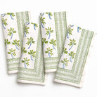 Set of four white napkins with green leaf patterns on a white background