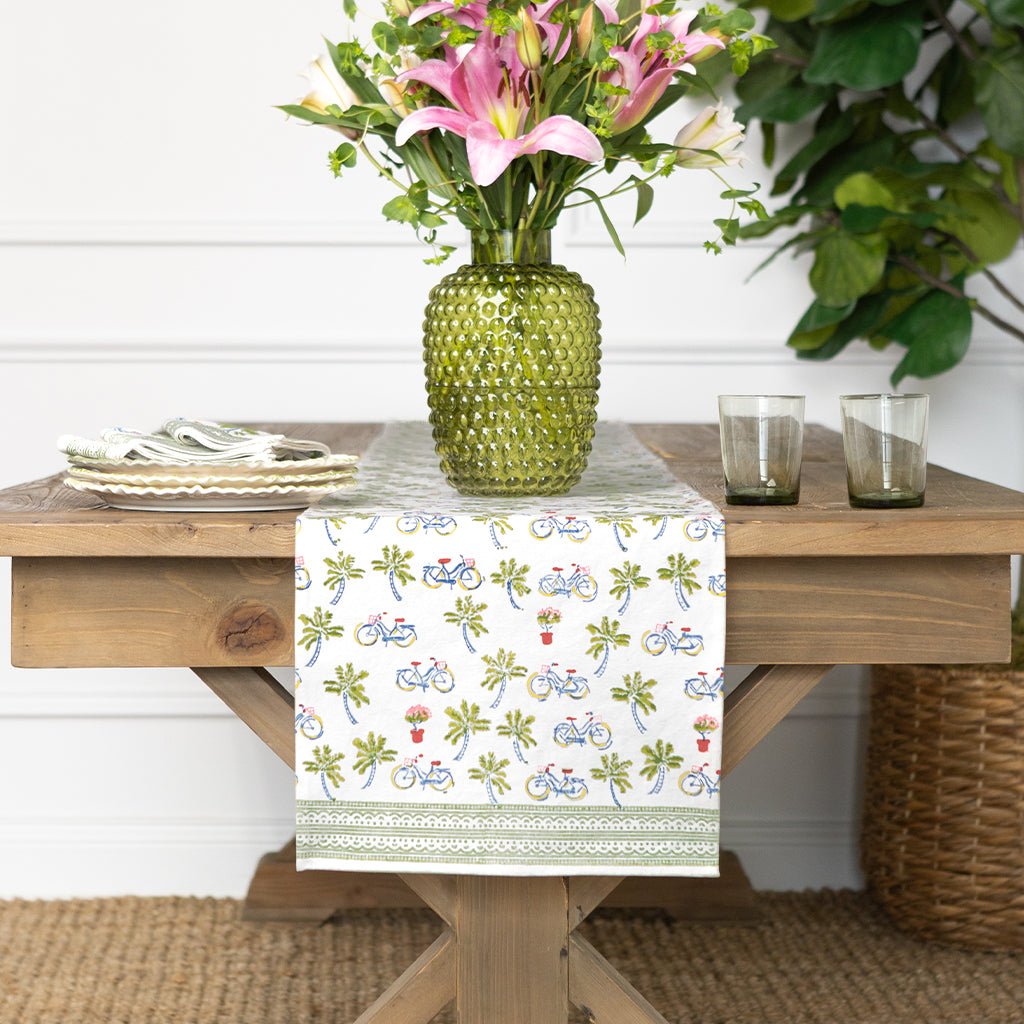 Dining table with a floral arrangement, green vase, and patterned table runner.