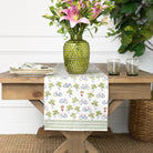 Dining table with a floral arrangement, green vase, and patterned table runner.