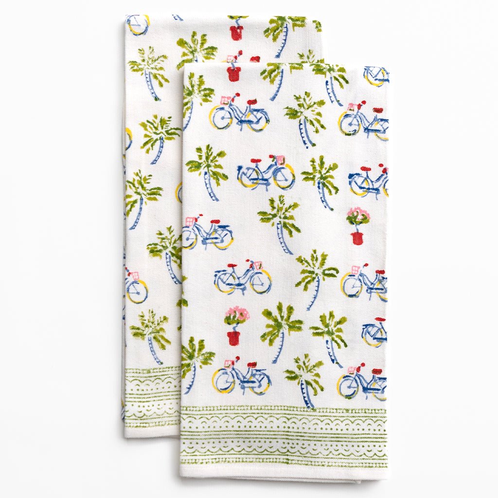 Two folded kitchen towels with bicycle and plant pattern on a white background