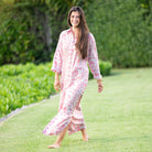 Woman in a pink floral dress walking on grass with greenery in the background