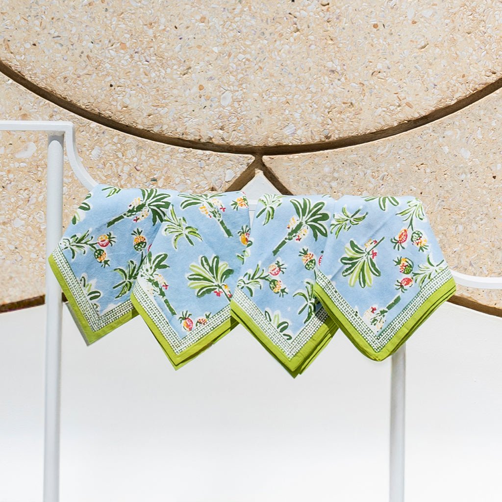 Set of four floral patterned napkins on a white stand against a beige stone wall.