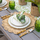 Table setting with green and white plates, cutlery, and glasses on a wooden table.