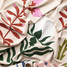 Close-up of fabric with floral patterns in red, green, and pink on a beige background.