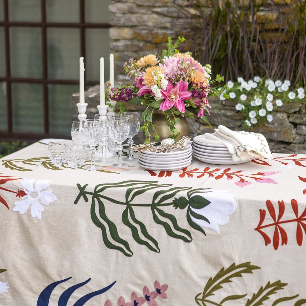 Decorated table with floral tablecloth, plates, glasses, and flowers outdoors.