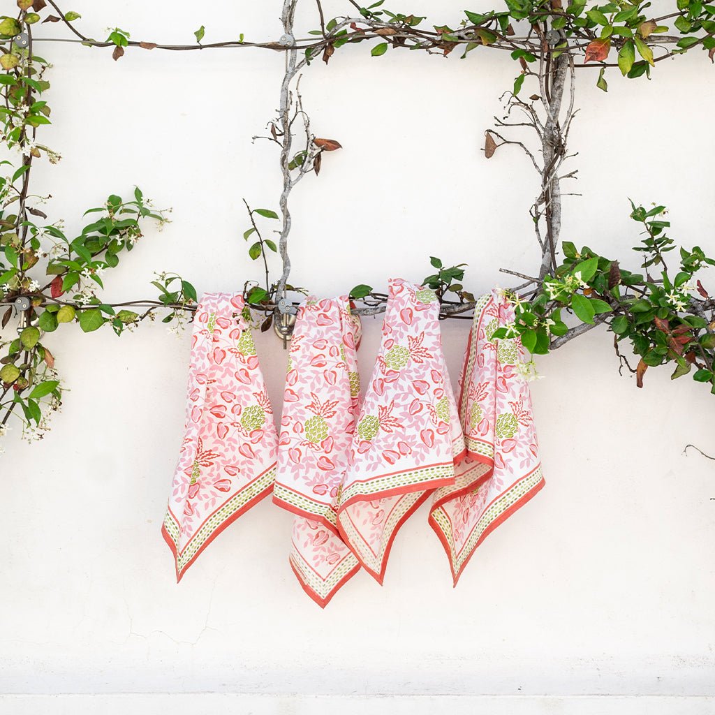 Three pink floral handkerchiefs hanging on a branch against a white wall.