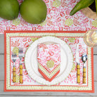Dinner setting with pink floral placemat, plates, and cutlery on a wooden table.