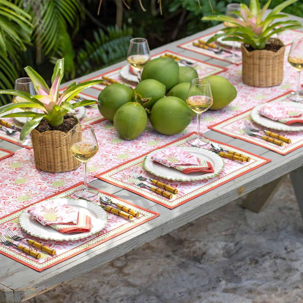 Outdoor table setting with green fruits, glasses, and floral napkins on a patterned tablecloth.