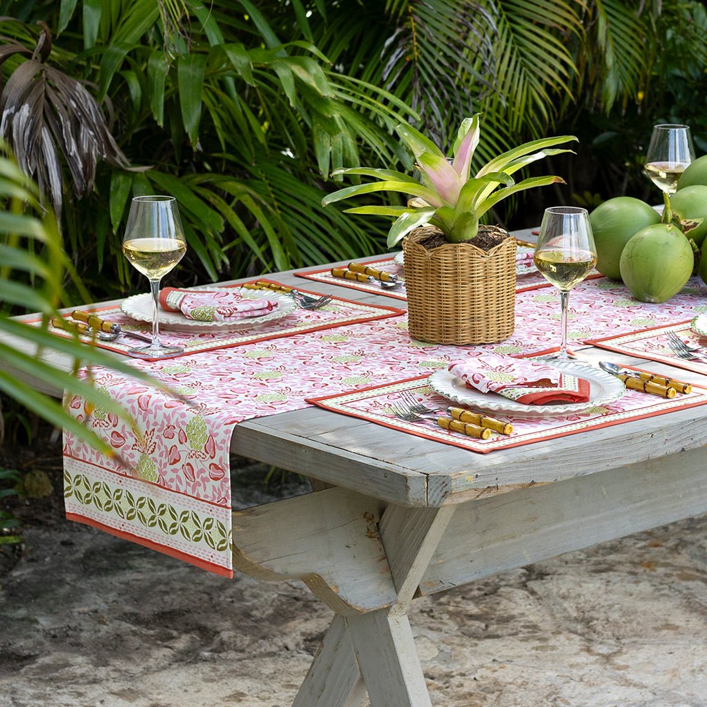 Outdoor table setting with a floral tablecloth, wine glasses, and tropical plants.