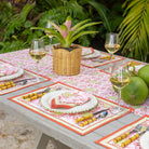 Outdoor table setting with floral tablecloth, glasses of white wine, and tropical plants.