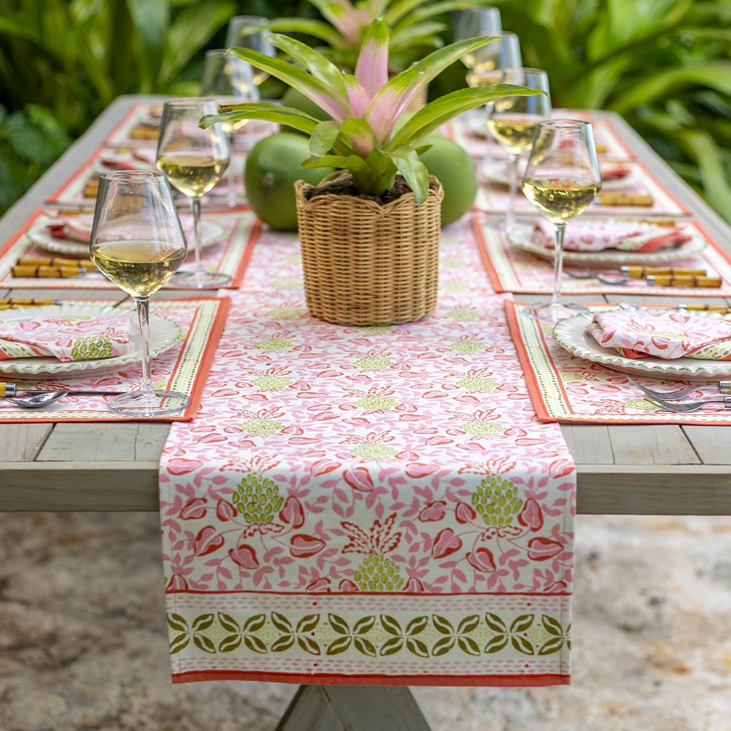 Outdoor table setting with a floral tablecloth, wine glasses, and a potted plant.