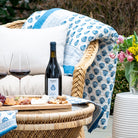 Outdoor setting with a wicker chair, blanket, bottle of wine, and platter of food.